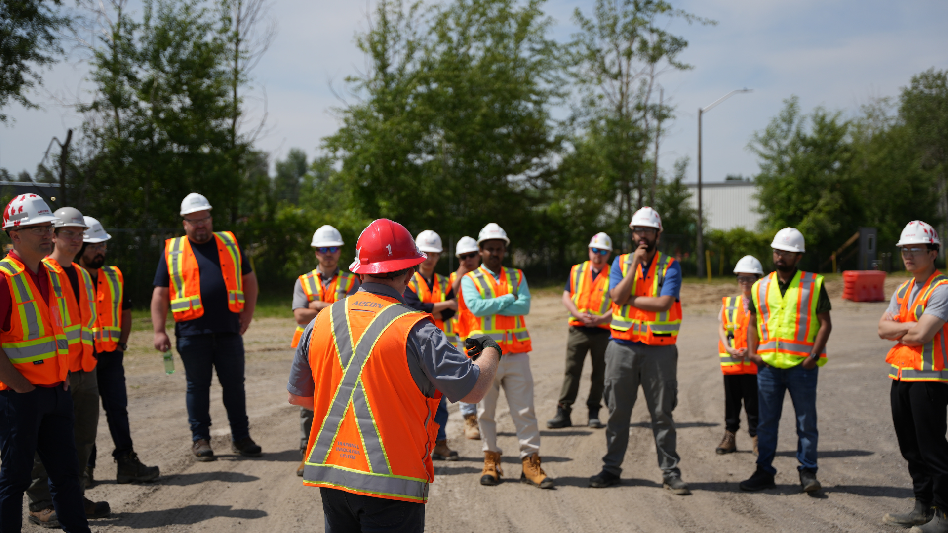 A group of employees in safety gear in a circle having a meeting outside